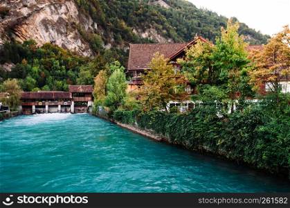 SEP 25, 2013 Interlaken, Switzerland - Turqouise water of Aare river and vintage Swiss style buildings along the shore in old town area with mountain background of Interlaken