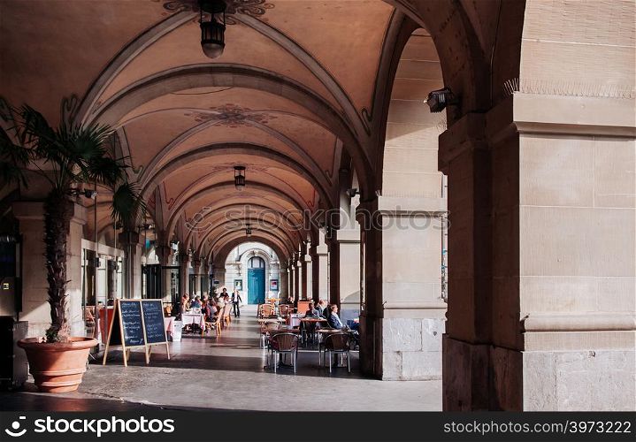SEP 27, 2013 Bern, Switzerland - European tourists having lunch in street restaurant with dinner table under arch arcade with sunlight in old town Bern.