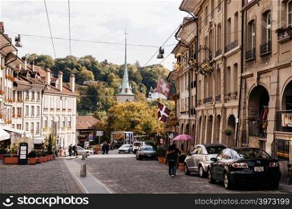 SEP 27, 2103 Bern, Switzerland - People walking on street among vintage historic Swiss style residential buildinfgs with Nydeggkirche Protestant church bell tower in old town Bern