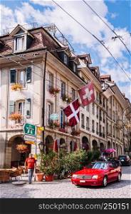 SEP 27, 2103 Bern, Switzerland - Red luxury car on Nydaggasse street, Swiss residential building with Swiss flag and street sign in Old town district of Bern