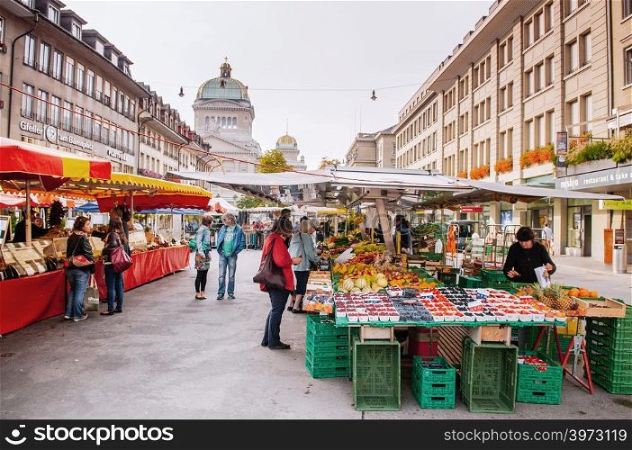 SEP 28, 2013 Bern, Switzerland - Swiss people buying fruit at local Vegetable and fruit shop in morning market Bundesplatz in front of Swiss Parliament building.