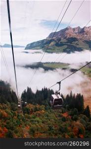 SEp 29, 2013 Engelberg, Switzerland - Ropeway Gondola flying over fog covered green pine forest alpine mountain valley of mount Titlis foot area.