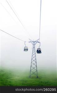 SEP 29, 2013 Engelberg, Switzerland - Ropeway Gondola flying over green grass field of foot of mount Titlis alpine mountain valley on foggy day.