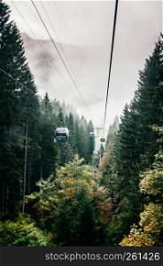 SEP 29, 2013 Engelberg, Switzerland - Ropeway Gondola flying over lush green pine forest in foot of mount Titlis alpine mountain valley on foggy day.