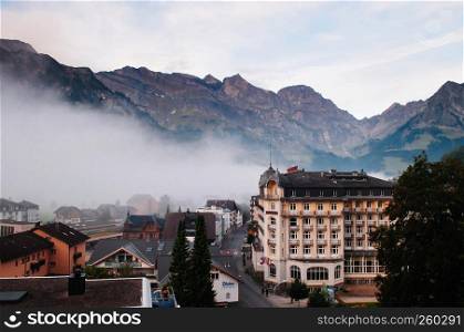 SEP 29, 2013 Engelberg, Switzerland - Swiss classic style chalet on quiet street with Swiss alps of Engelberg town in early autumn on foggy day