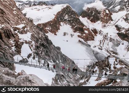 SEp 29, 2013 Engelberg, Switzerland - Tourists walking on Cliff walk suspension bridge on top of mount Titlis, 500 meters above snow mountain valley famous attraction of Swiss alps.