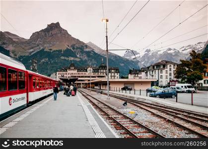 SEP 29, 2013 Engelberg, Switzerland - Tourists with luggages and train at Engelberg station platform with Swiss alps mountain rang in background during autumn season