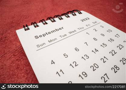 September 2022 - spiral desktop calendar against red handmade paper, low angle macro shot, time and business concept