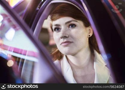 Serene businesswoman opening car door at night, close-up, reflected lights