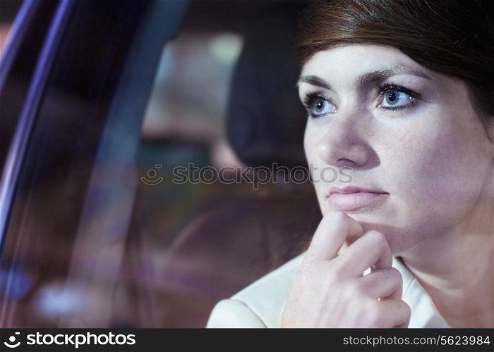 Serene businesswoman with hand on chin looking through car window at the city nightlife, reflected lights