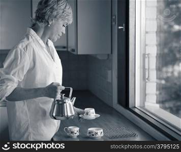 Serene morning moment, mature woman drinking coffee in the kitchen, sunlight coming from the window