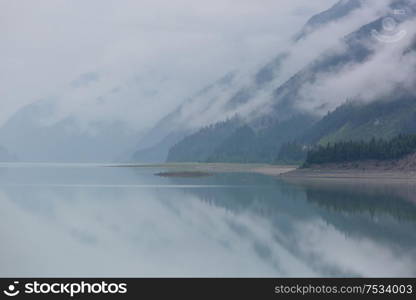 Serene scene by the mountain lake in Canada with reflection of the rocks in the calm water.