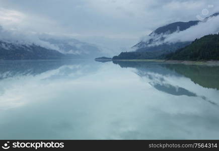 Serene scene by the mountain lake in Canada with reflection of the rocks in the calm water.