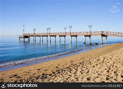 Serene scenery of a sandy beach and a wooden pier on Costa del Sol between resort town of Marbella and Puerto Banus in Spain, Malaga province