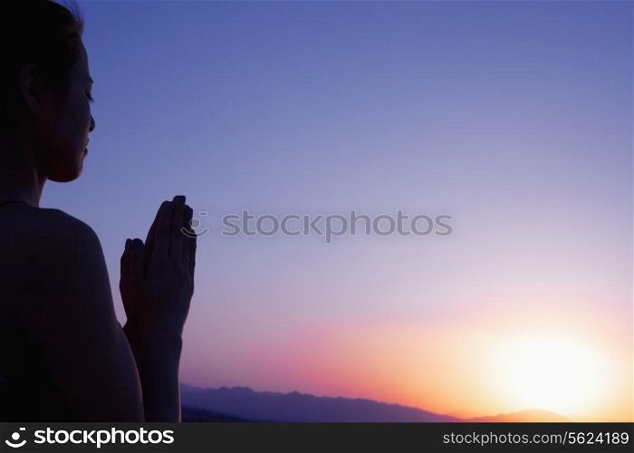 Serene young woman with hands together in prayer pose in the desert in China, silhouette, sun setting