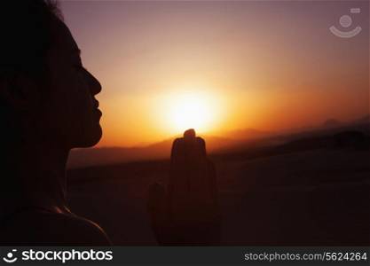 Serene young woman with hands together in prayer pose in the desert in China, silhouette, sun setting