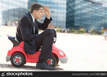 Serious Adult Businessman sitting in the with Little Red Toy Car and Trying to See his Way