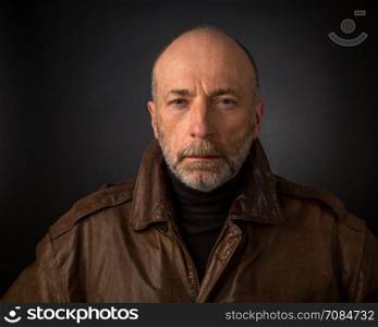 serious and focused senior man in leather jacket - a headshot against a black background