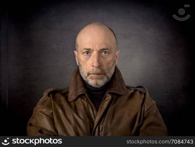 serious and focused senior man in leather jacket - a headshot against a dark grunge background
