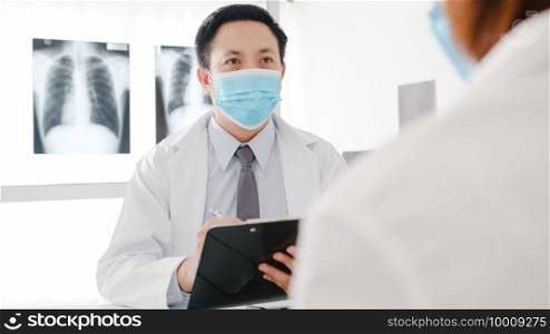Serious Asia male doctor wear protective mask using clipboard is delivering great news talk discuss results or symptoms with female patient in hospital office. Lifestyle new normal after corona virus.