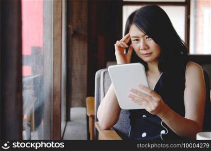Serious Asian businesswoman is reading and having a headache with online news on tablet at modern office. Healthy and technology concept.