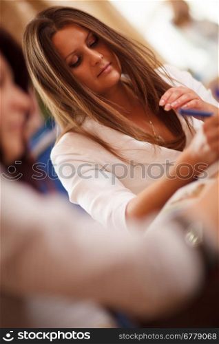 Serious beautiful young businesswoman in a meeting writing notes, tilted view past the shoulder of a female colleague