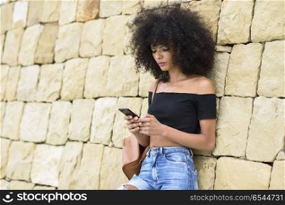 Serious black woman looking at her smart phone outdoors. Serious black woman with afro hair looking at her smart phone outdoors. Lifestyle concept