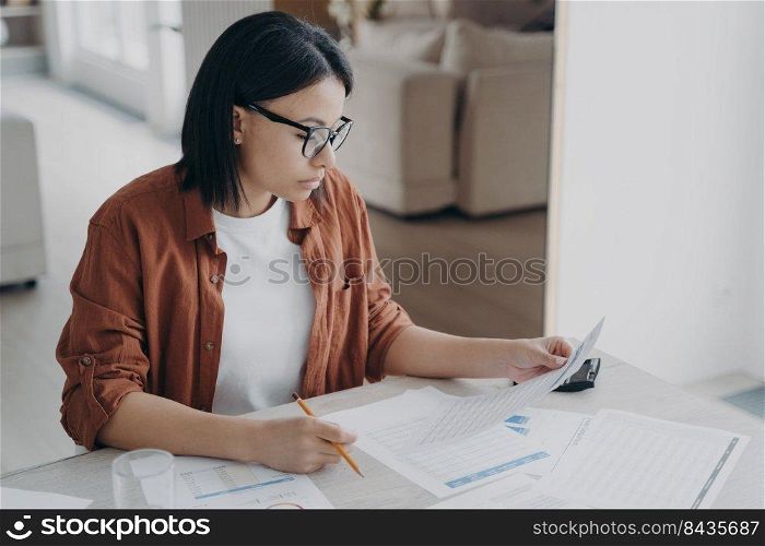 Serious business lady is examining documents. Young caucasian woman working remote from home. Manager or entrepreneur doing paperwork. Concept of intelligent professional and business strategy.. Serious business lady is examining documents. Intelligent professional and business strategy.