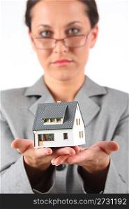 serious business woman in glasses holds model of house