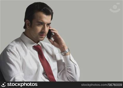 Serious businessman answering smart phone over gray background