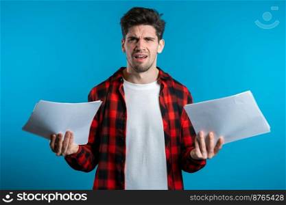 Serious businessman boss on blue background. He is unsatisfied, anxious and confused with work of staff. Young male office employee checks documents, reports.. Serious businessman boss on blue background. He is unsatisfied, anxious confused