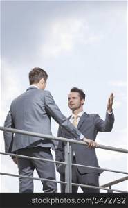 Serious businessman gesturing while looking at coworker against sky