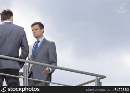 Serious businessman looking at coworker against clear sky