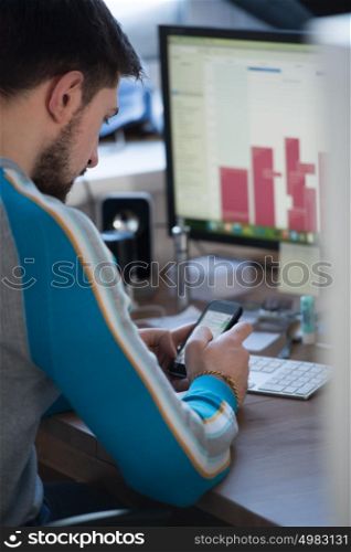 Serious businessman sitting in office and working with phone and computer
