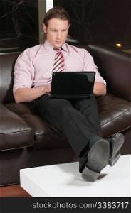 Serious businessman sitting on couch and working on laptop computer