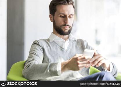 Serious businessman texting on mobile phone while sitting at office
