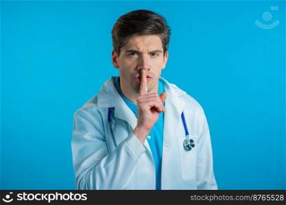 Serious doctor man in white coat holding finger on lips over blue background. Gesture of shhh, secret, silence. Close up. High quality photo. Serious doctor man in white coat holding finger on lips over blue background. Gesture of shhh, secret, silence. Close up.