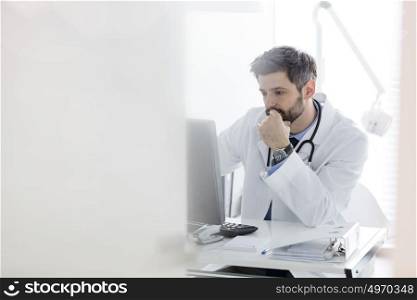 Serious doctor using computer at desk in hospital