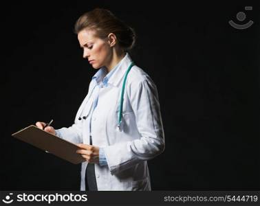 Serious doctor woman writing in clipboard isolated on black