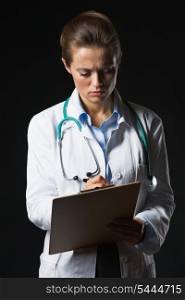 Serious doctor woman writing in clipboard on black background