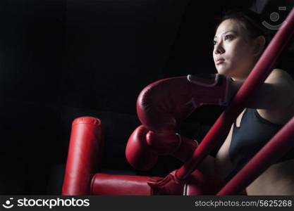 Serious female boxer resting her elbows on the ring side, looking away, low angle view