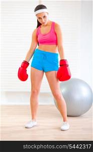 Serious fit woman in boxing gloves standing in angry pose at living room&#xA;
