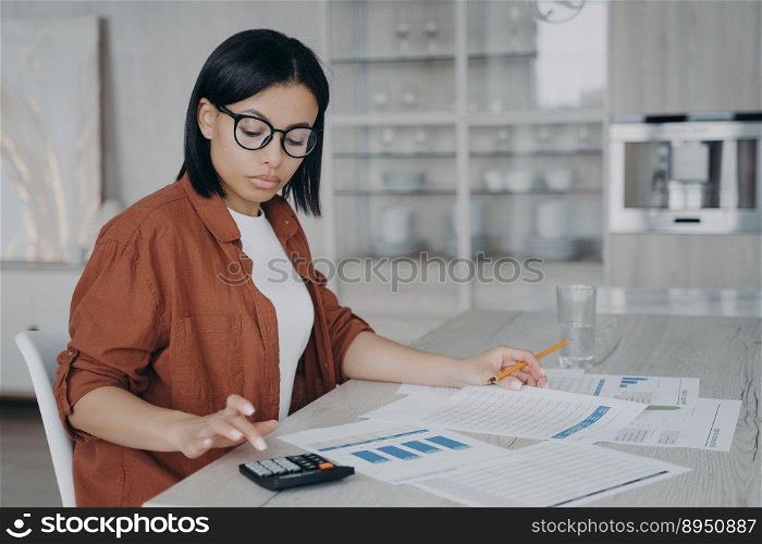 Serious girl, accountant is examining reports. Young european woman in glasses is working with data charts from home. Manager or business assistant is sitting at the desk and doing business.. Accountant examining reports. Business assistant in glasses is working with data charts from home.