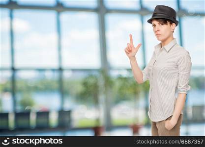 serious girl holds fingers pistol and wears a black hat in the office