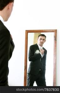 Serious handsome bridegroom looking in mirror straightening his tie