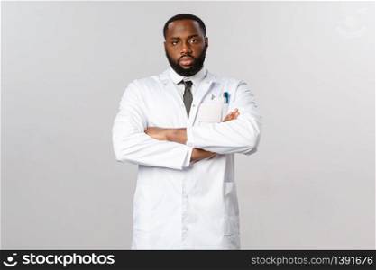 Serious-looking disappointed african-american doctor looking skeptical and tired at person not following covid-19 quarantine recommendations, cross arms chest, staring camera, wear white coat.. Serious-looking disappointed african-american doctor looking skeptical and tired at person not following covid-19 quarantine recommendations, cross arms chest, staring camera, wear white coat