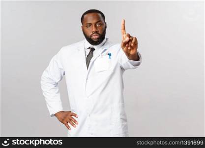 Serious-looking handsome african-american doctor in white coat, shaking index finger in warning, prohibit outdoor activitiy covid19 pandemic outbreak, disease spreading, tell stay home be safe.. Serious-looking handsome african-american doctor in white coat, shaking index finger in warning, prohibit outdoor activitiy covid19 pandemic outbreak, disease spreading, tell stay home be safe