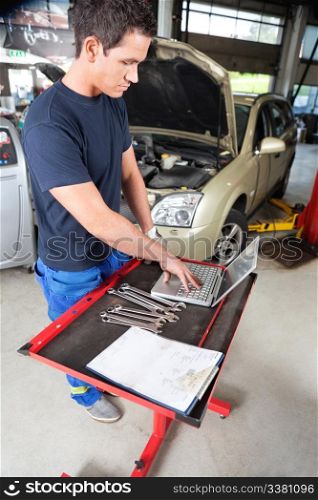 Serious looking mechanic working on a laptop in garage