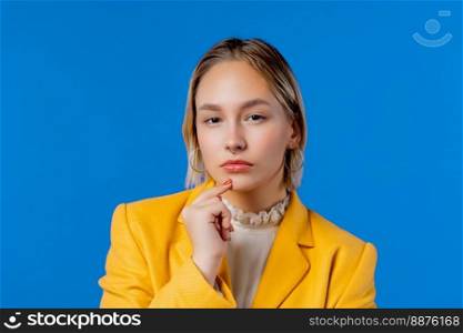 Serious looking suspicious woman in yellow on blue background. Curious, looks with disbelief, doubts. High quality photo. Serious looking suspicious woman in yellow on blue background.Curious, disbelief