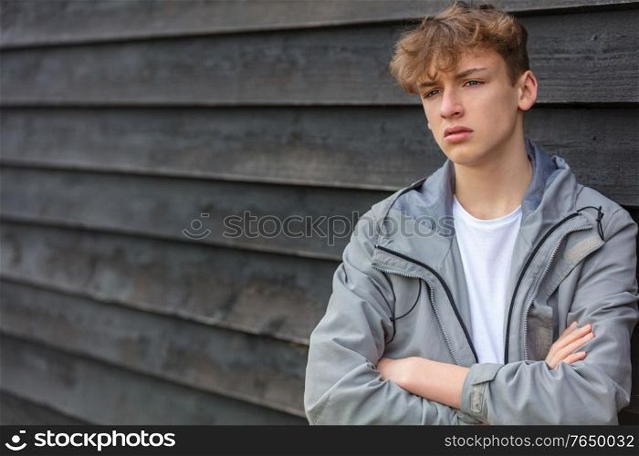 Serious male boy teenager outside leaning against a wall wearing looking sad, moody, thoughtful or depressed